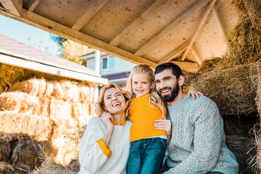 Personal Insurance - Portrait of a Cheerful Family with a Young Daughter Sitting on Hay in a Farm Building at Home